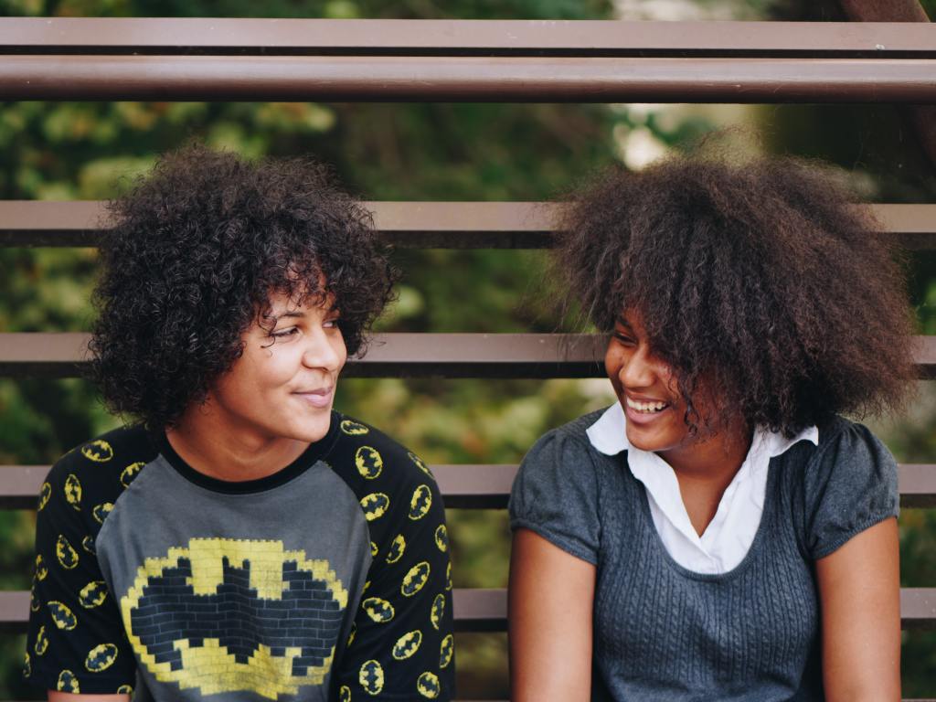 two mixed-race American kids with curly hair sitting and laughing together