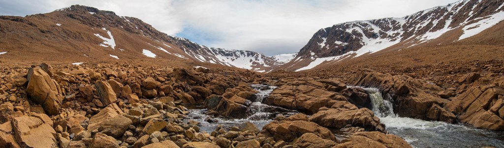 the red and brown stones and snowy mountains with a stream and waterfall, the tablelands in Newfoundland and Labrador