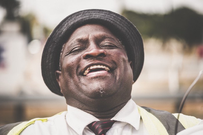 upper middle-aged black man with a hat smiles in laughter